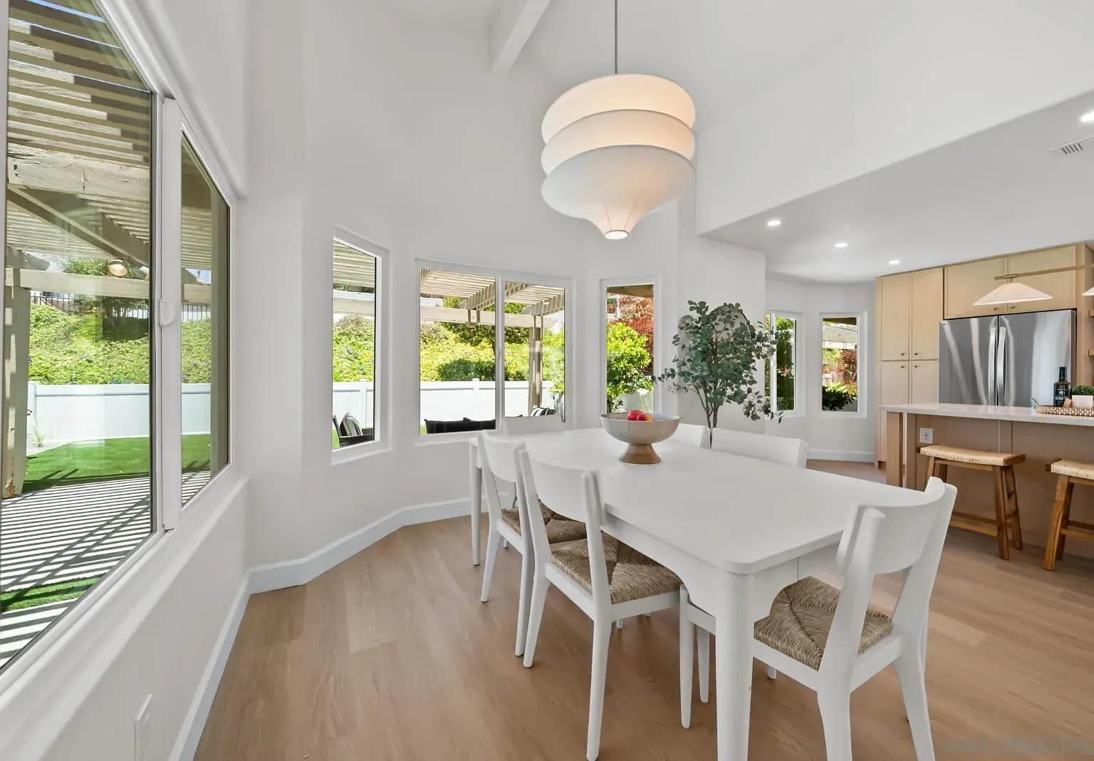 The dining nook at 4742 Collinos Way, with a white table for six, a paper drum pendant, and sliding doors looking out to the new turf and covered pergola